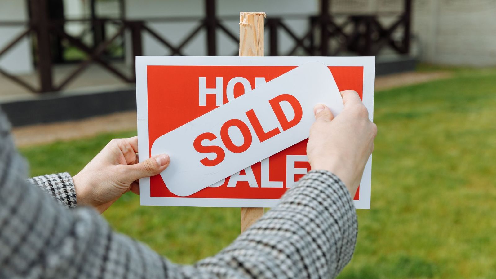 Des mains apposant un autocollant Vendu sur un panneau immobilier