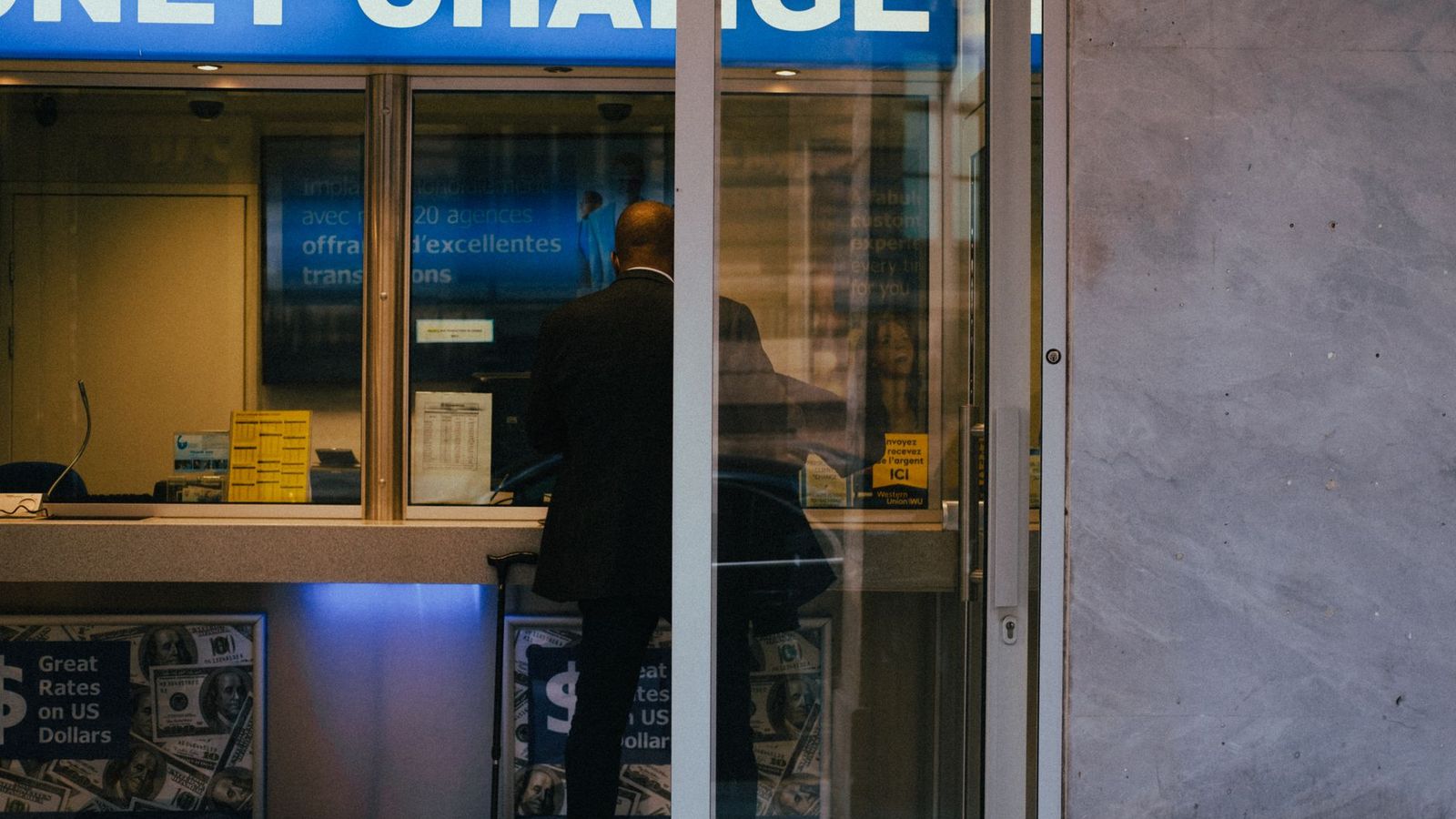 Un homme au guichet d'un bureau de change, les taux affichés derrière la vitre